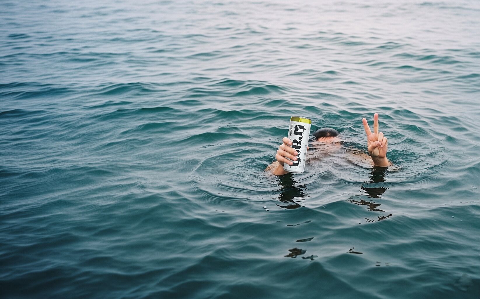 A swimmer holding up a TRASH can and a peace sign in the sea